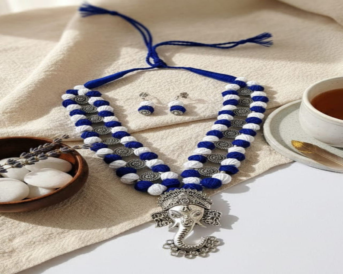 Blue and white beaded necklace with silver pendant on a beige fabric background