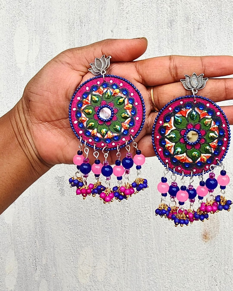 Colorful embroidered earrings held in a hand against a light background