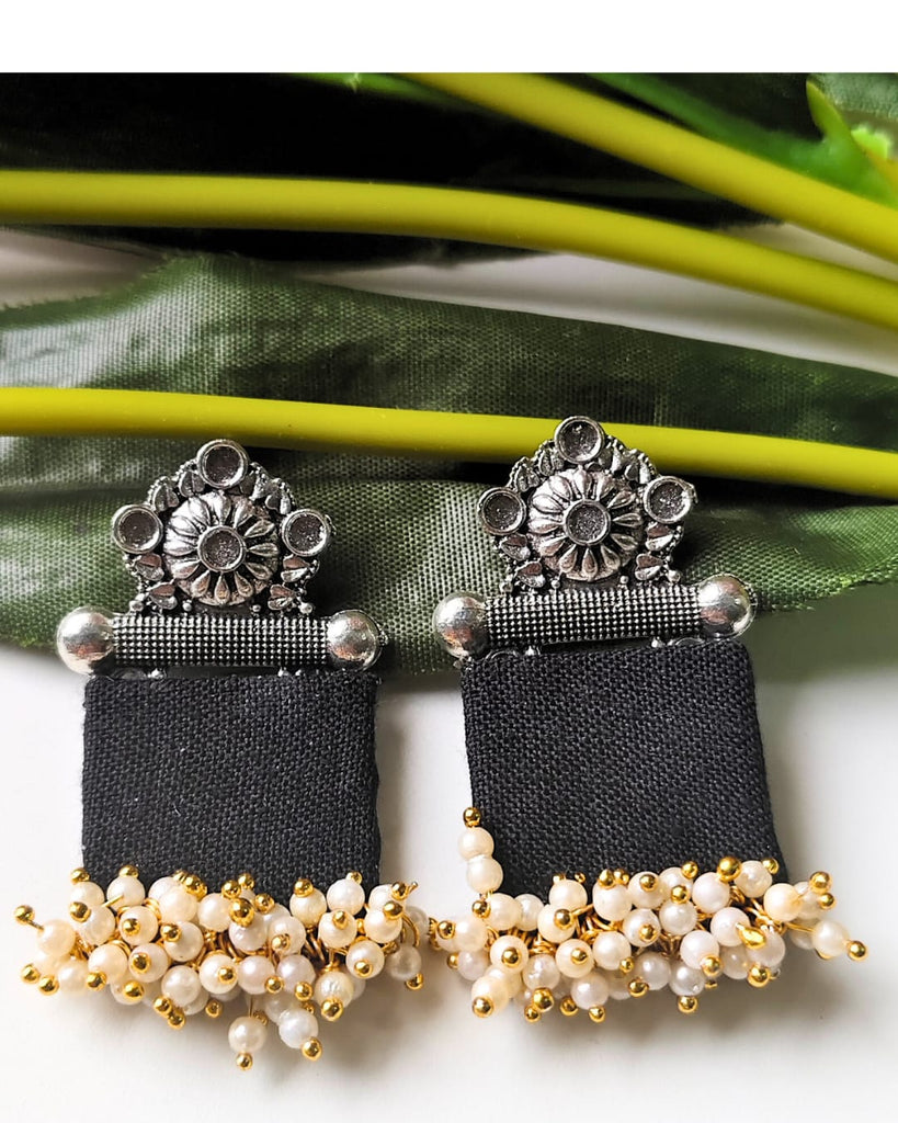 Pair of black earrings with silver and gold accents on a green leaf background