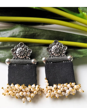 Pair of black earrings with silver and gold accents on a green leaf background