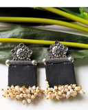 Pair of black earrings with silver and gold accents on a green leaf background
