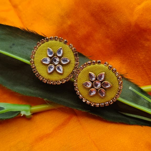 Pair of earrings with floral design on a green leaf against an orange fabric background