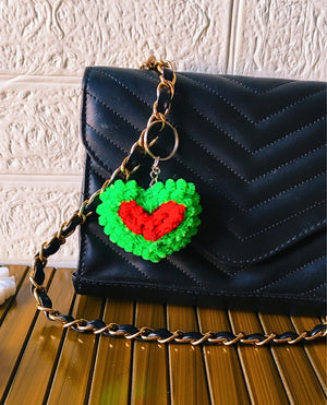 Green and Red heart-shaped Pipe Cleaner keychain on a wooden surface.