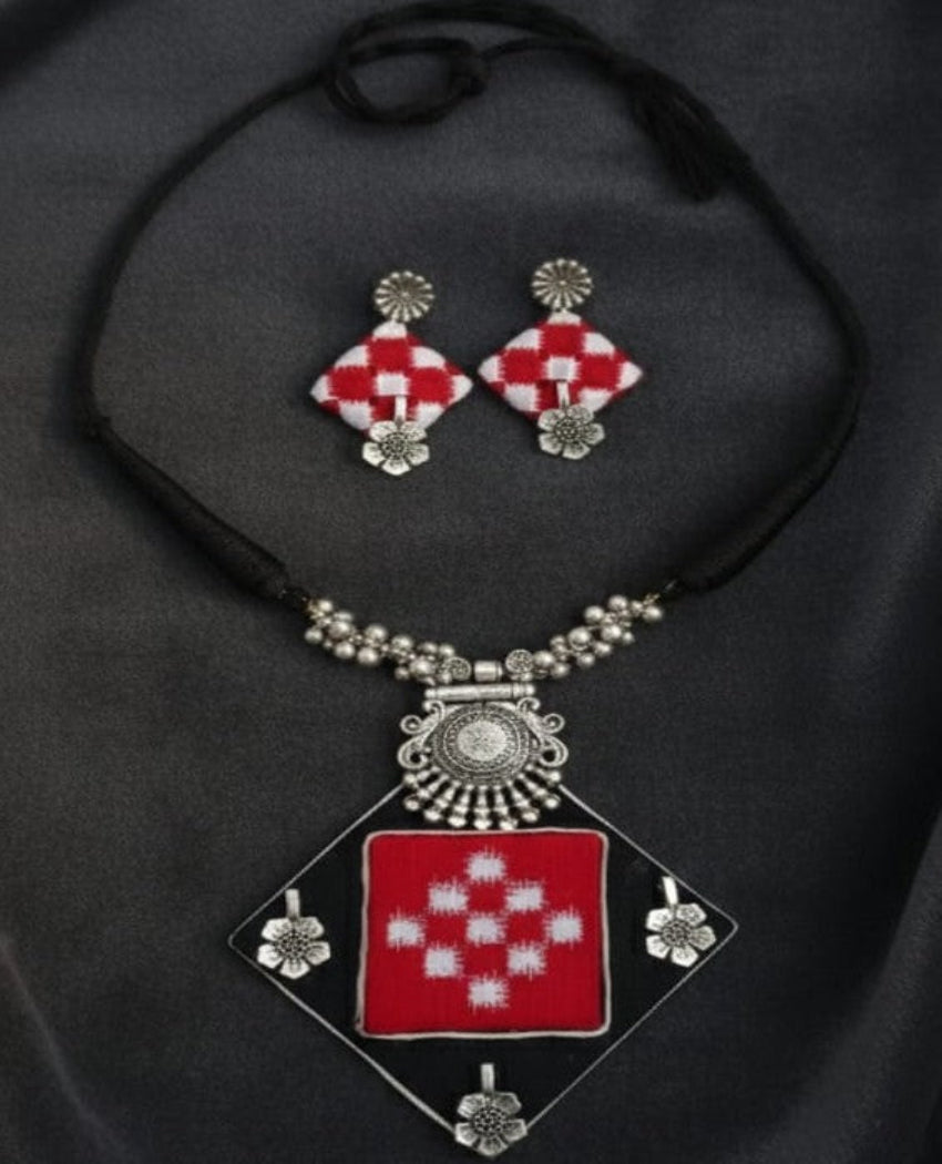 Necklace and earrings with red and white geometric design on a black background