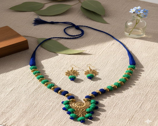 Necklace and earrings set with blue and green beads on a textured surface with leaves and flowers.